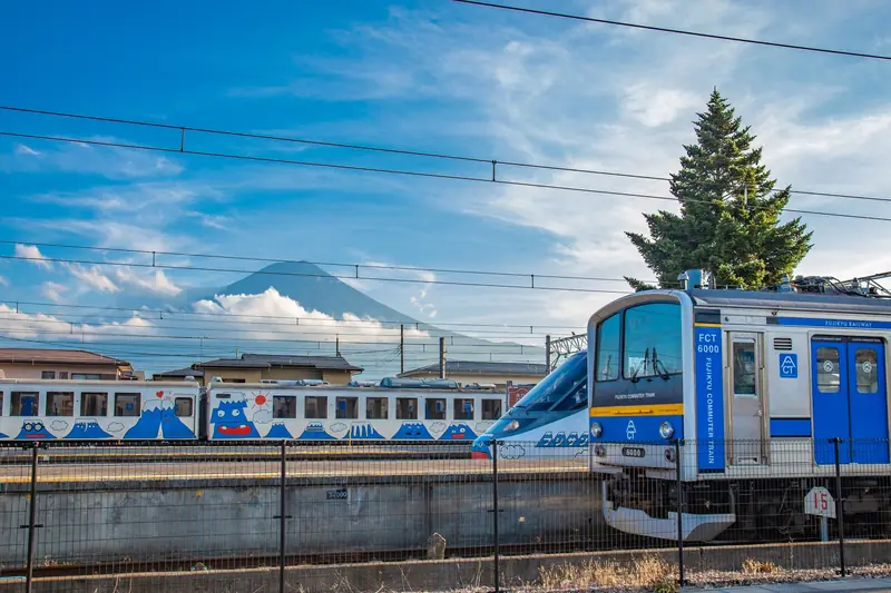 A train passing below a snow-capped Mount Fuji under a clear blue sky