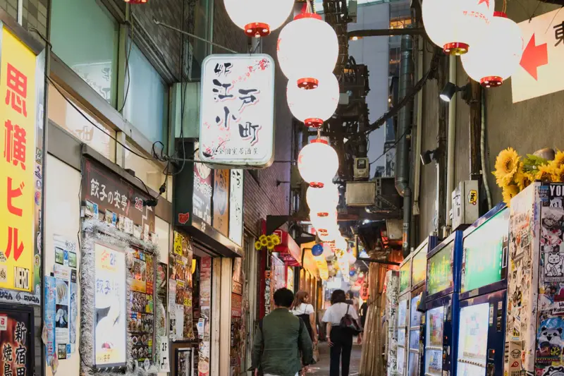 A narrow Tokyo yokocho alley at night lit by paper lanterns