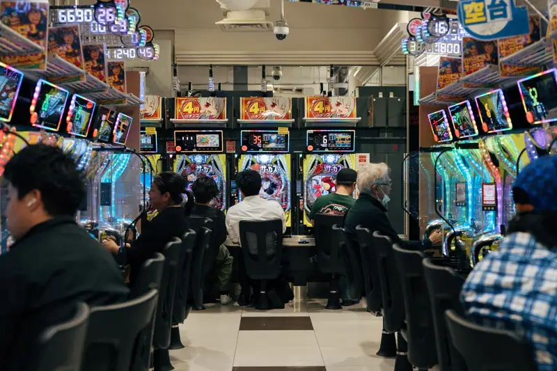 Rows of brightly lit pachinko machines with adults playing in a Japanese parlour