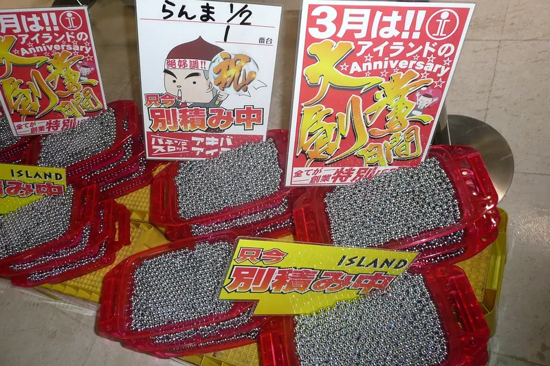 Red trays piled high with steel pachinko balls under handwritten prize signs in a Tokyo hall