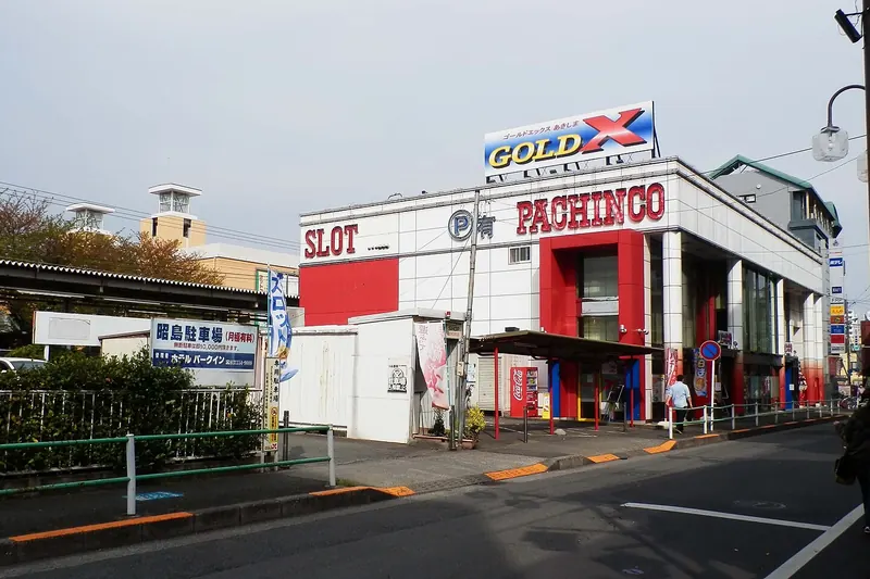 A large pachinko and slot parlour building with red and white signs on a street in Akishima, Tokyo